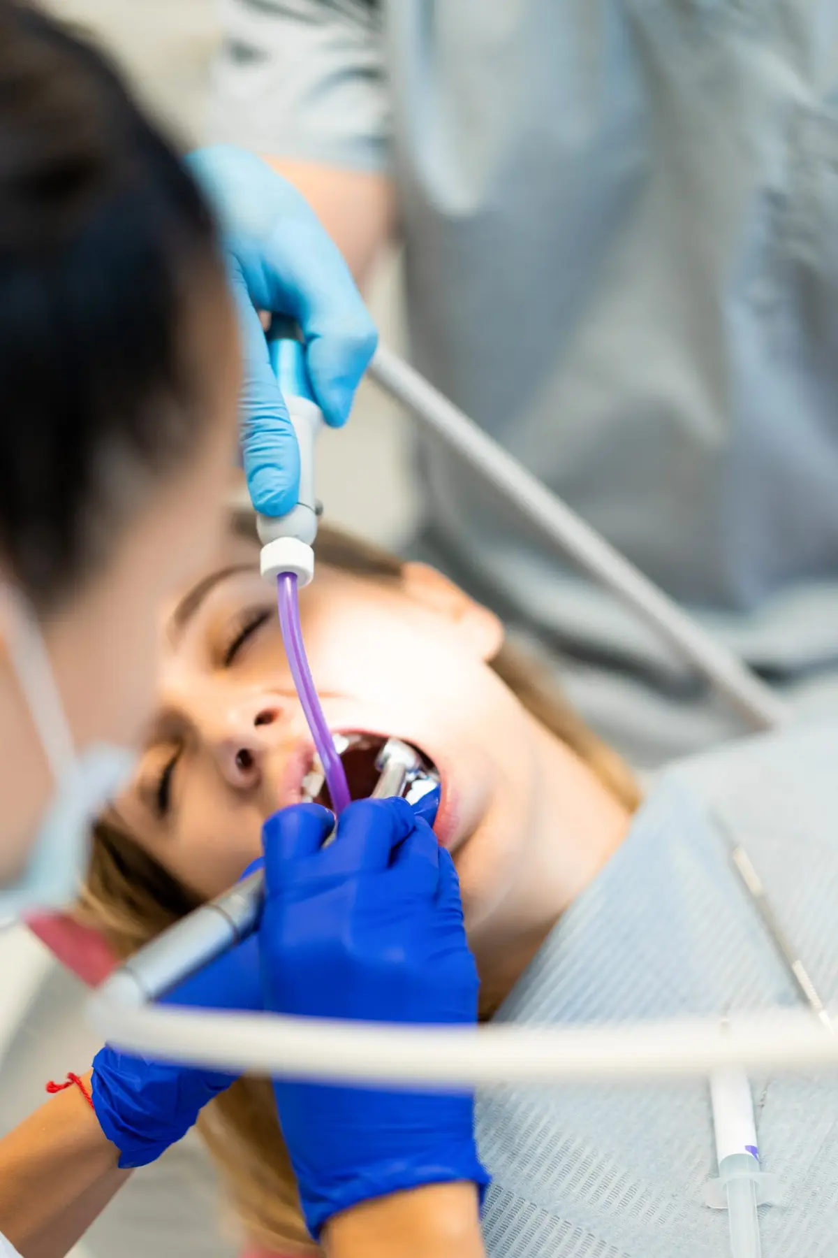 A patient lying back with her mouth open while a gloved hand holds a suction tip and a mirror inside it